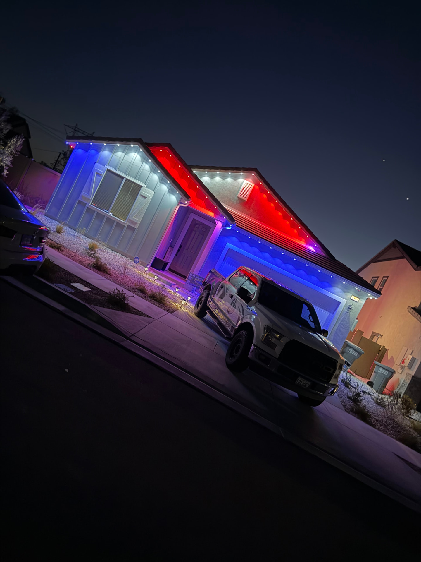 Home lit in red, white and blue permanent LED lighting with a work truck in the driveway