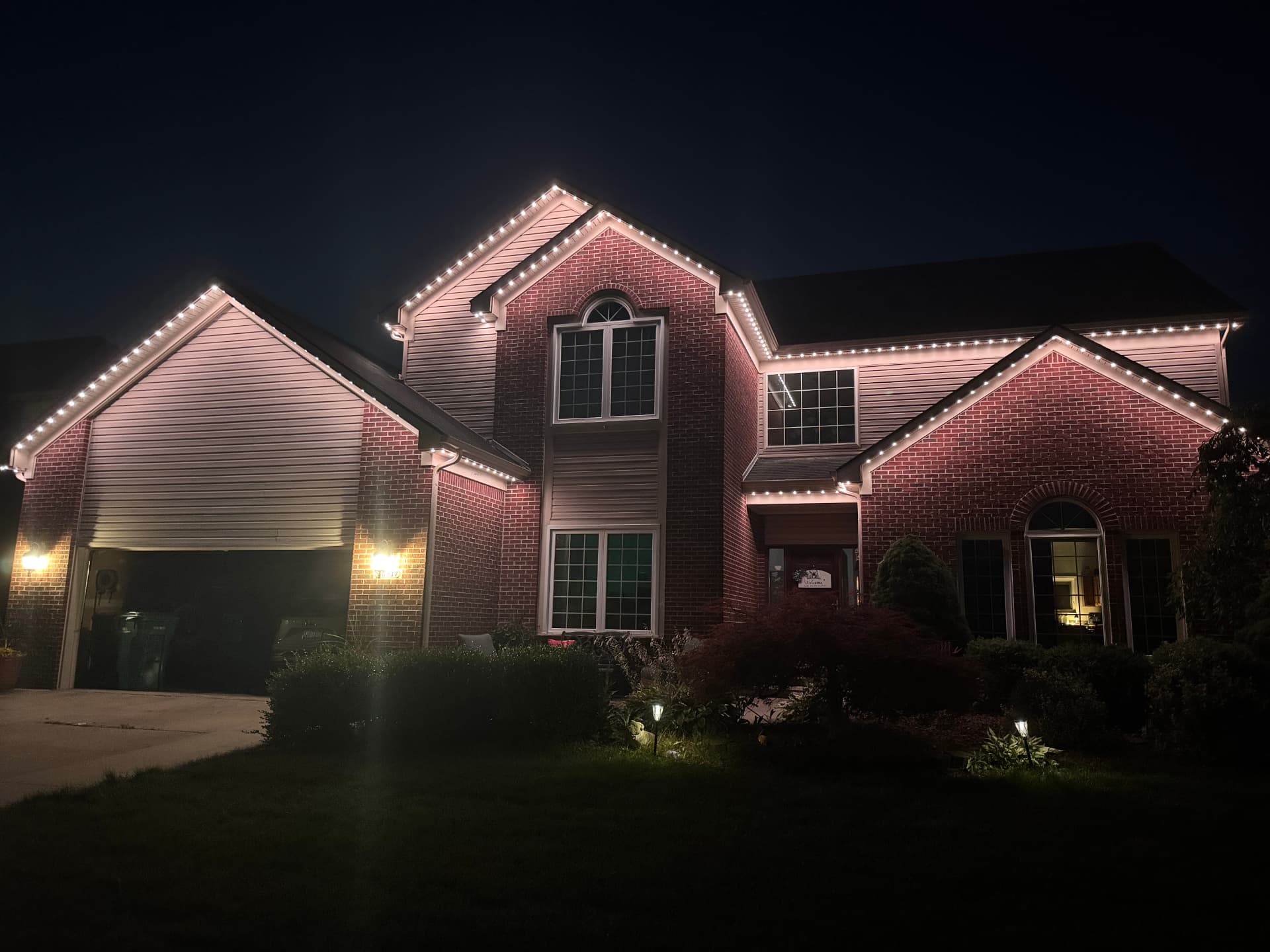 Brick two-story home with warm white permanent LED lighting tracing every roofline